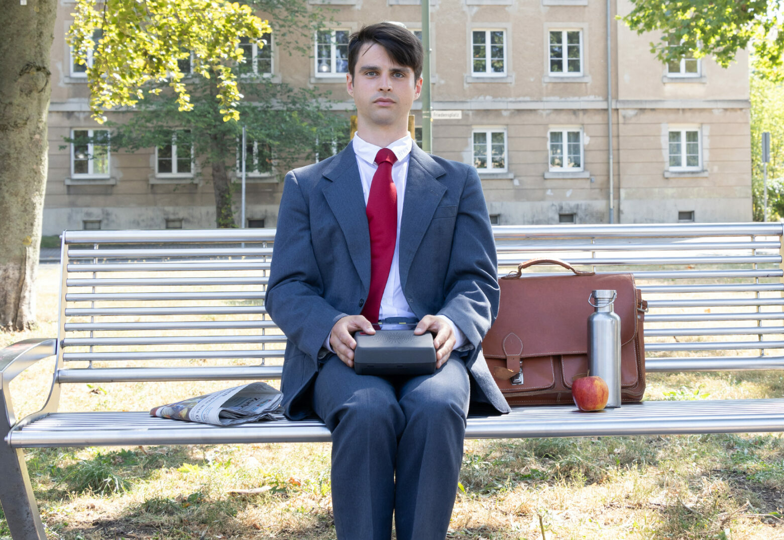 Eric Bernardy sitzt auf einer Parkbank und hält einen Kassetenrekorder auf dem Schoss als wäre er Forrest Gump mit seiner Pralinenschachtel.